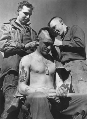 Robert Capa, Un paracadutista statunitense si fa tagliare i capelli nello stile degli Indiani d'America prima di una missione degli Alleati nei pressi del Reno, Arras - Francia (Photo by Robert Capa/Getty Images)