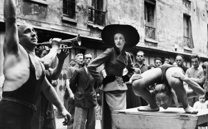 Elise Daniels with street performers, suit by Balenciaga, Le Marais, Paris, 1948. Photograph by Richard Avedon © The Richard Avedon Foundation