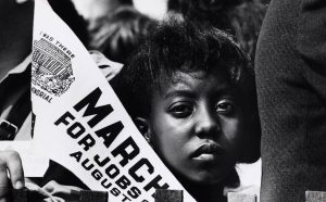 Fotografia di una giovane donna alla Marcia per i diritti civili a Washington, DC con uno stendardo. 28 agosto 1963 Washington, D.C., USA Autore sconosciuto © Courtesy U.S. Information Agency - Press and Publications Service / NARA - National Archives and Records Administration